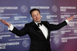 Elon on a red carpet posing for cameras while wearing an elegant suit