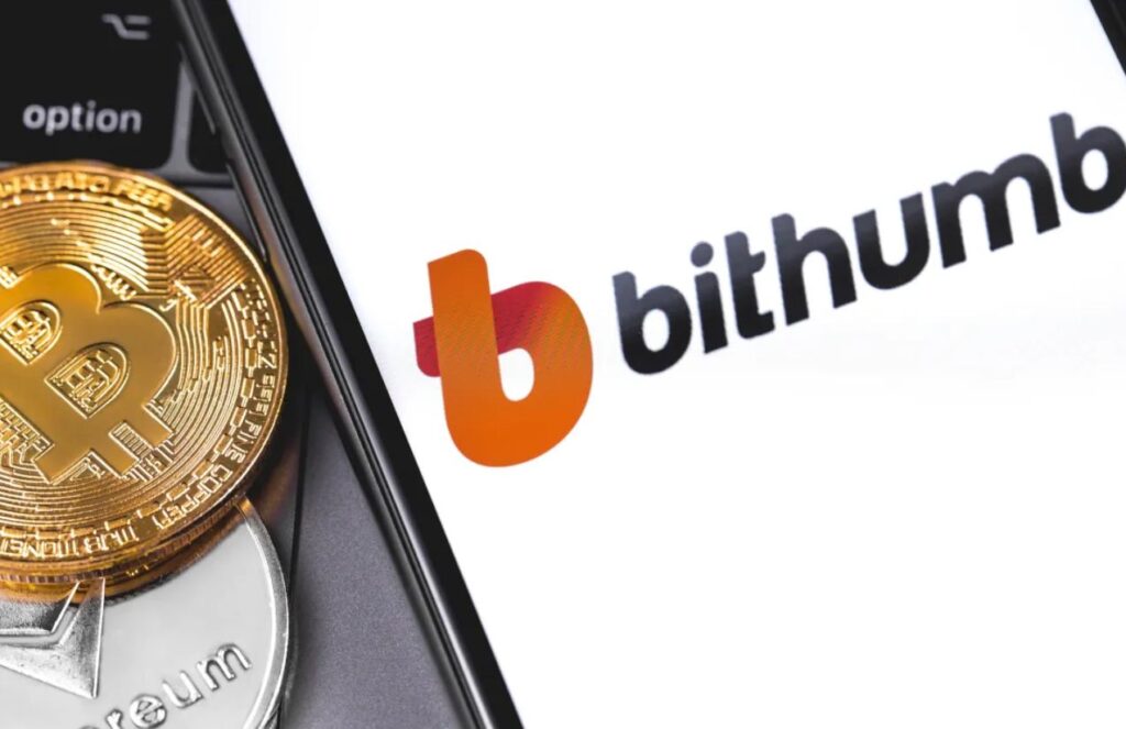 A cellphone opening the Bithumb platform, with several bitcoin coins next to it