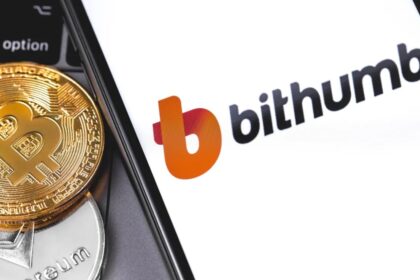 A cellphone opening the Bithumb platform, with several bitcoin coins next to it