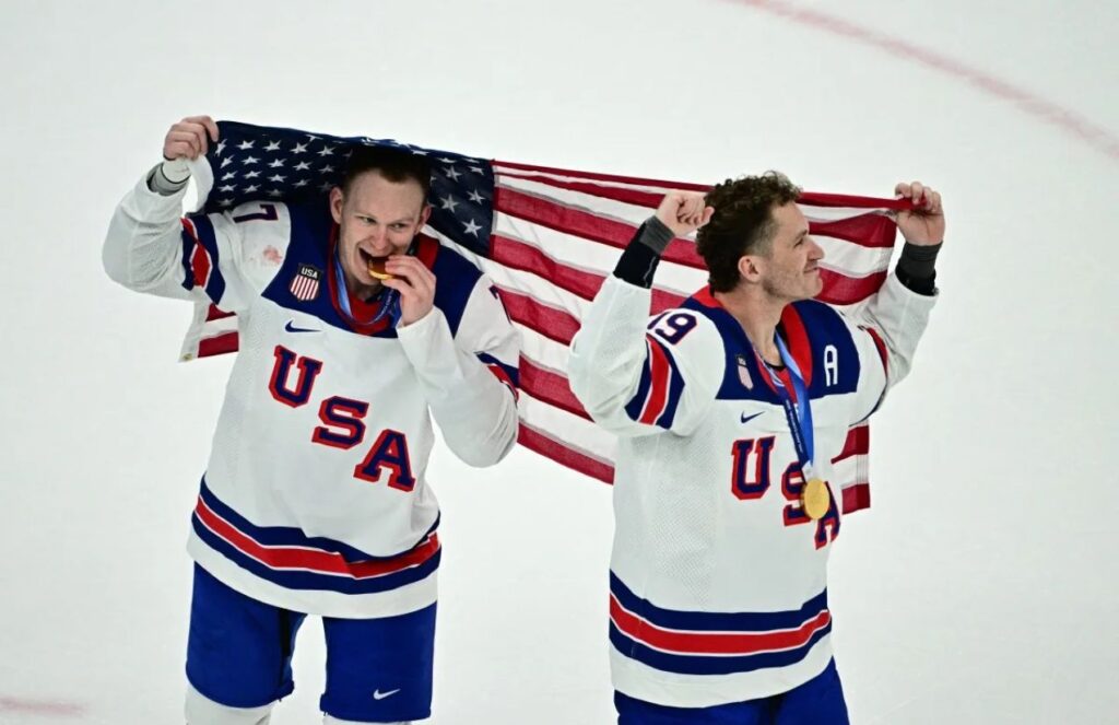 Historic olympic gold: United States ends 46-year drought, defeats canada in hockey Two players from the U.S. hockey team celebrating with their country’s flag and gold medals hanging around their necks