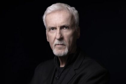 James Cameron posing in an elegant suit against a black background