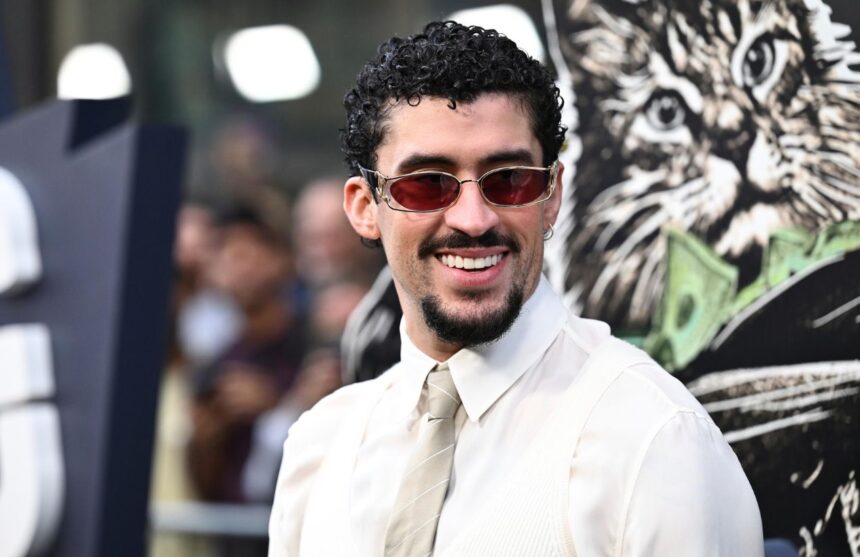 Bad Bunny posing for the cameras on a red carpet in an elegant and eye-catching white suit with shiny accessories
