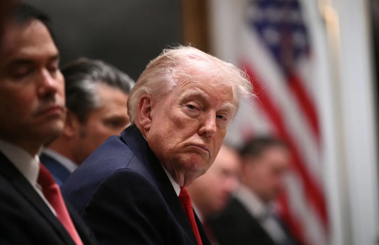 Trump sitting with several politicians, wearing a very serious expression and an intimidating posture