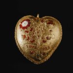 A gold jewel shaped like a heart, with red carvings that appear to be made of ruby