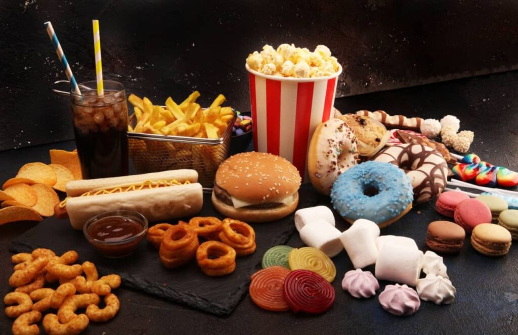 Three everyday foods that can harm your kidneys A table displaying several junk food dishes and sugary drinks