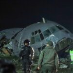 A completely destroyed airplane with several emergency service personnel surrounding the area and securing the scene