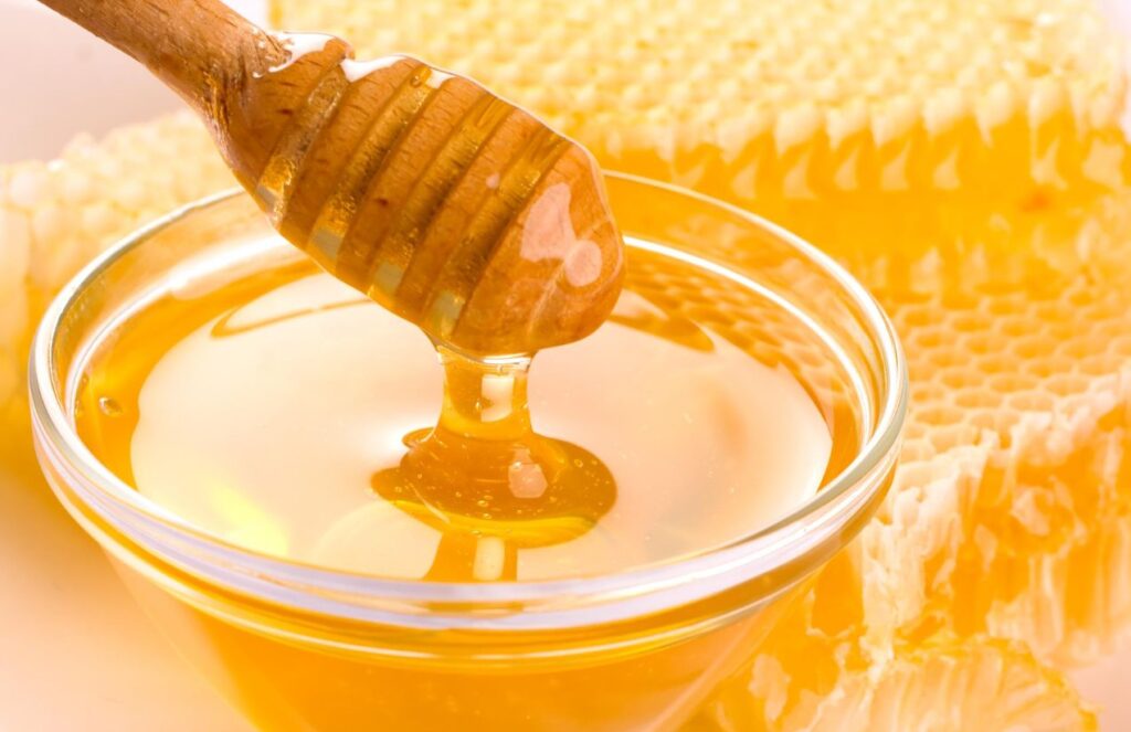 A bowl of honey with a spoon scooping some of the viscous substance