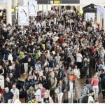 An airport crowded with people walking around, looking for their flights, and others waiting to board