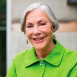 Alice with short white hair, wearing a green blouse and smiling for the cameras