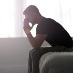 A silhouette of a man sitting on the edge of a bed with a sad posture