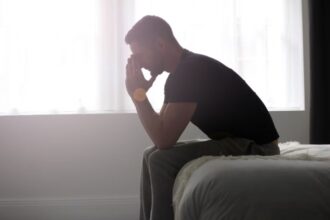 A silhouette of a man sitting on the edge of a bed with a sad posture
