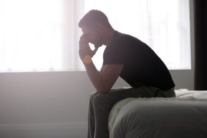 A silhouette of a man sitting on the edge of a bed with a sad posture