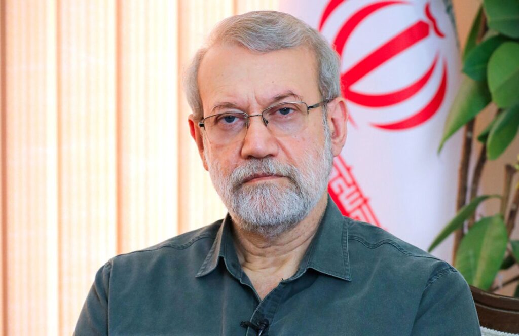 The deceased leader posing for a photo in his office with an Iranian flag behind him
