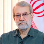The deceased leader posing for a photo in his office with an Iranian flag behind him