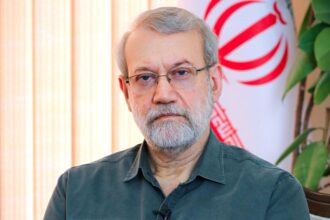 The deceased leader posing for a photo in his office with an Iranian flag behind him