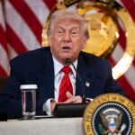 Trump sitting in a meeting with a soccer ball and the World Cup trophy beside him