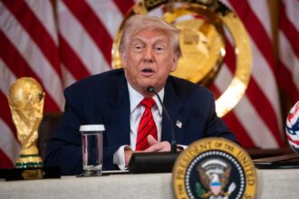 Trump sitting in a meeting with a soccer ball and the World Cup trophy beside him