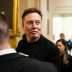 Elon Musk walking with a smile in what appears to be the White House