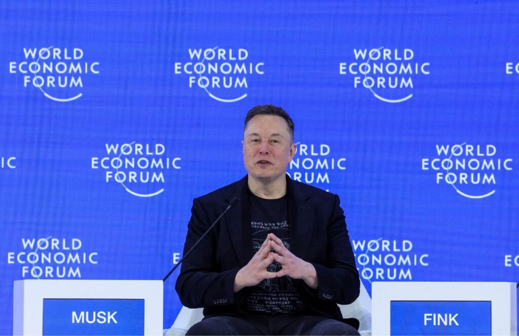 Elon sitting in the middle of a forum, speaking with his followers and visitors