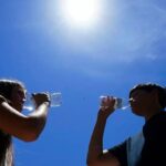 Two people drinking bottles of water after the intense heat wave hitting them