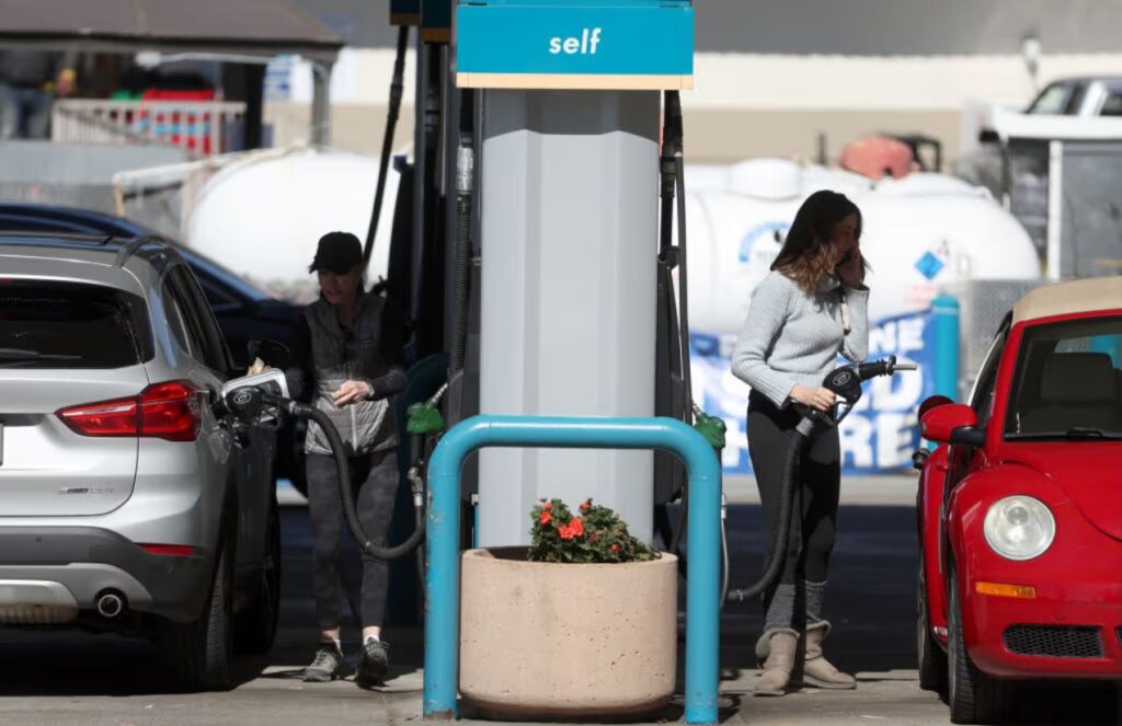 A gas station with two people fueling their cars on each side of the pump