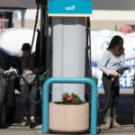 A gas station with two people fueling their cars on each side of the pump