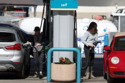 A gas station with two people fueling their cars on each side of the pump