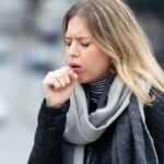 A woman holding her chest while coughing outdoors
