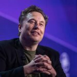 Elon Musk sitting in an armchair during a debate with many people in the audience