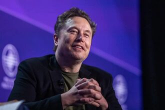 Elon Musk sitting in an armchair during a debate with many people in the audience