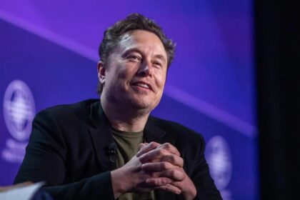 Elon Musk sitting in an armchair during a debate with many people in the audience