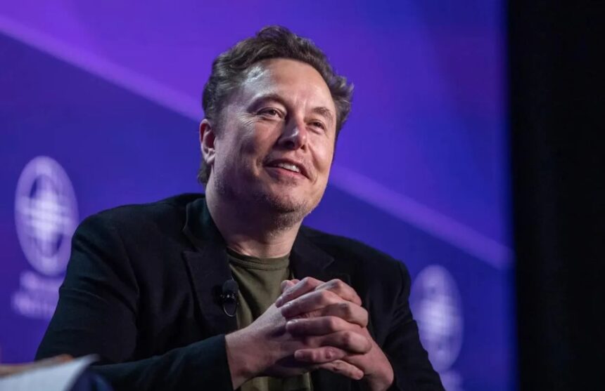 Elon Musk sitting in an armchair during a debate with many people in the audience