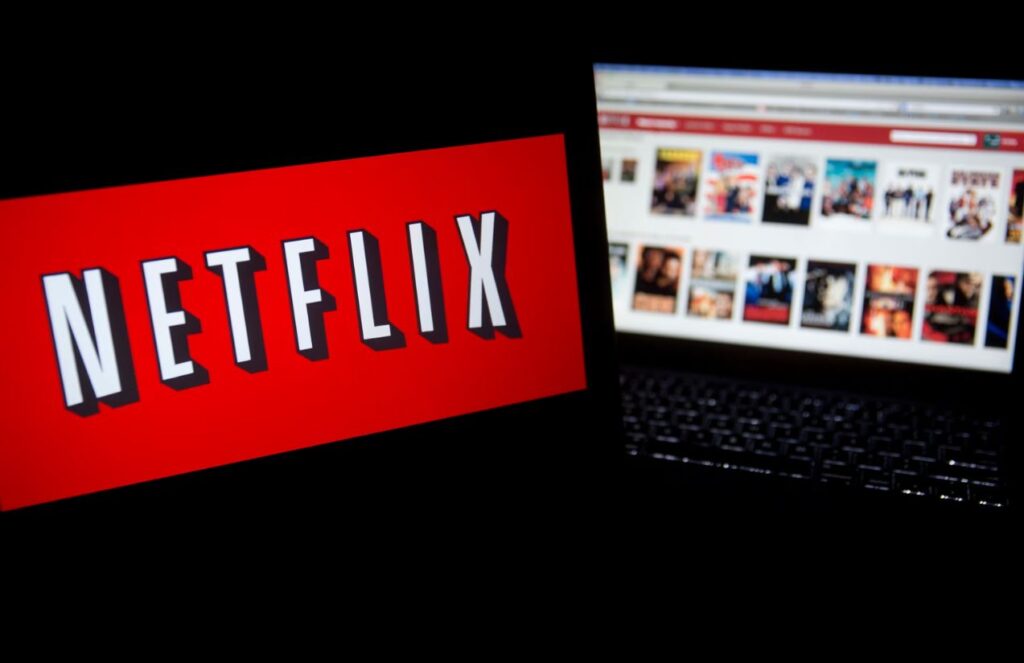 A dark room with two screens, one displaying the Netflix logo and the other showing the full catalog of the streaming platform