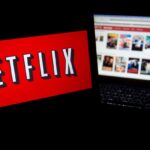 A dark room with two screens, one displaying the Netflix logo and the other showing the full catalog of the streaming platform