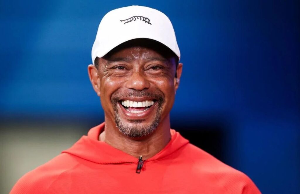 Mr. Tiger Woods wearing red and smiling widely at a golf event