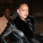 Rihanna wearing a black coat in the middle of the street while being photographed by photographers