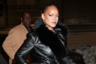 Rihanna wearing a black coat in the middle of the street while being photographed by photographers
