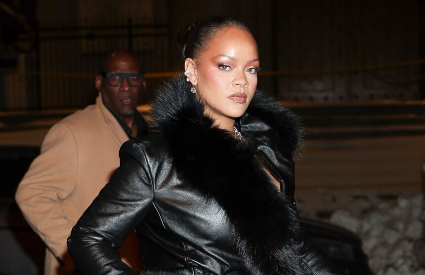 Rihanna wearing a black coat in the middle of the street while being photographed by photographers