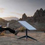 A person sitting and using their computer with a Starlink antenna next to them