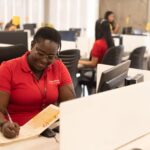 A woman working at a call center in her office while writing in a notebook
