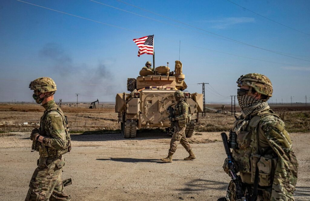 The United States deploys troops to regain control of the Strait of Hormuz Several soldiers walking with their equipment while being escorted by a tank