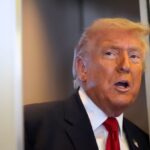 Donald Trump peeking out from a doorway wearing an elegant suit