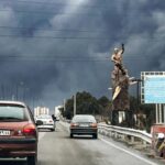 Many cars driving along a highway on a day with little sunlight and very dense clouds or fog in the sky