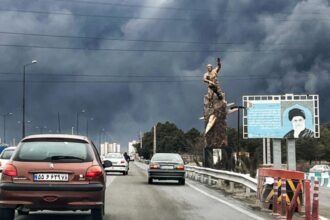 Many cars driving along a highway on a day with little sunlight and very dense clouds or fog in the sky