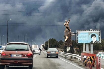 Many cars driving along a highway on a day with little sunlight and very dense clouds or fog in the sky