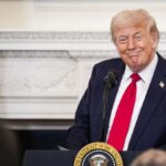 Donald Trump wearing an elegant suit speaking behind a podium.