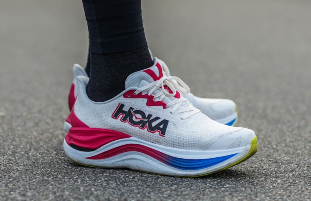 A pair of beautiful white HOKA shoes with red and blue details.