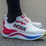A pair of beautiful white HOKA shoes with red and blue details.