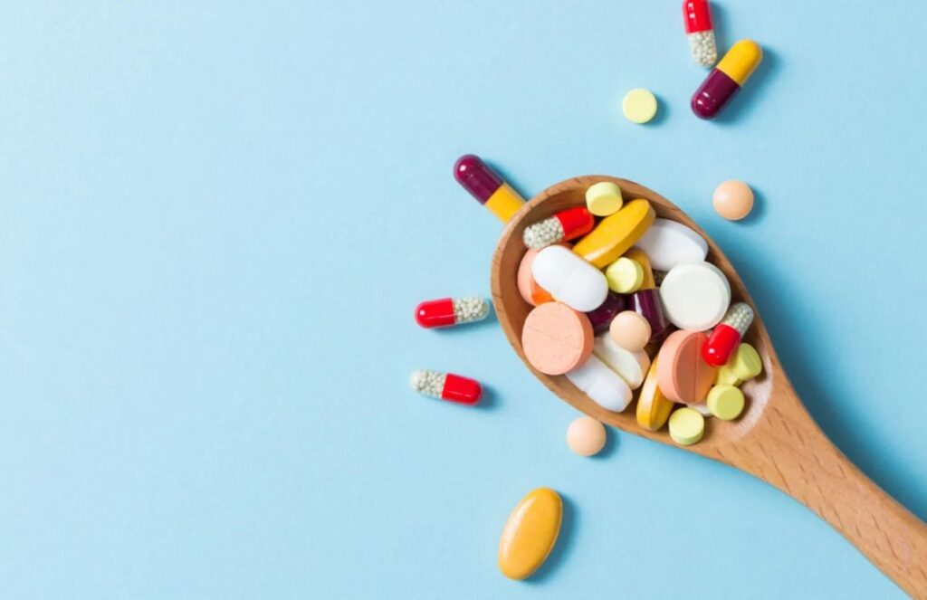 A spoon filled with multiple pills and vitamins, overflowing beyond it.