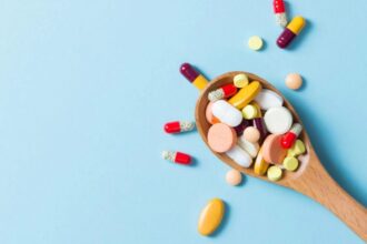 A spoon filled with multiple pills and vitamins, overflowing beyond it.